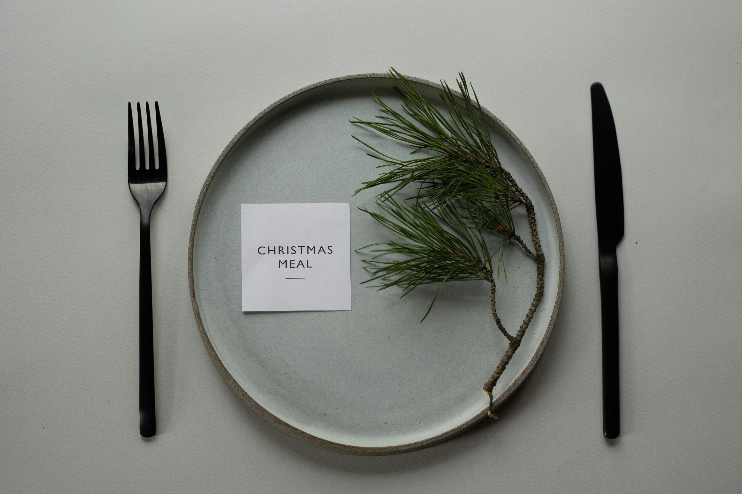 Top view arrangement of plate and cutlery served on dining table with pine twig and card with inscription Christmas Meal